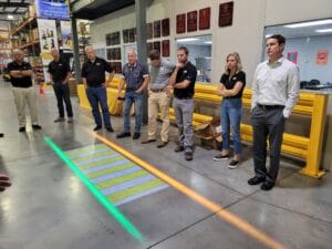 A group of people standing in a warehouse learning about forklift warning lights.