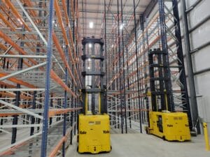 Two yellow forklifts in a warehouse with shelves, ready for loading and unloading goods.
