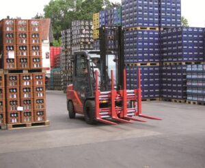 Forklift with two sets of forks driving in between pallets of product stacked high outside.