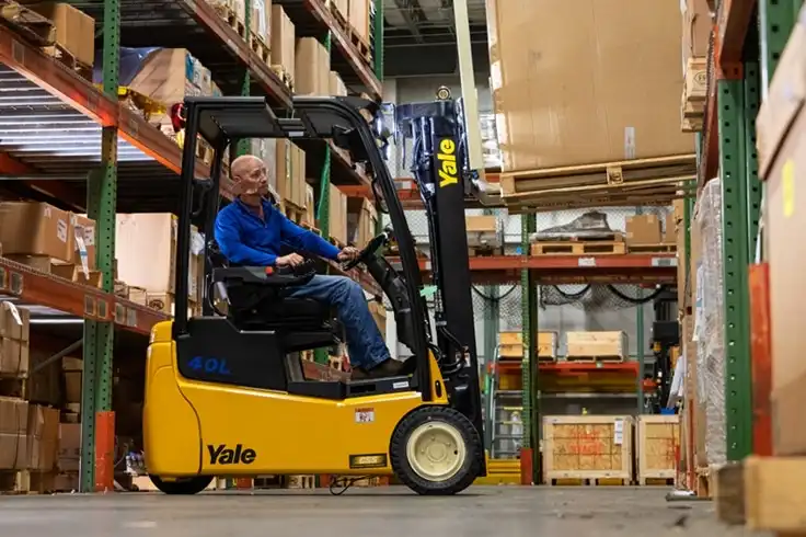 A forklift operator using a Yale electric forklift to lift a load from pallet racking in a warehouse.