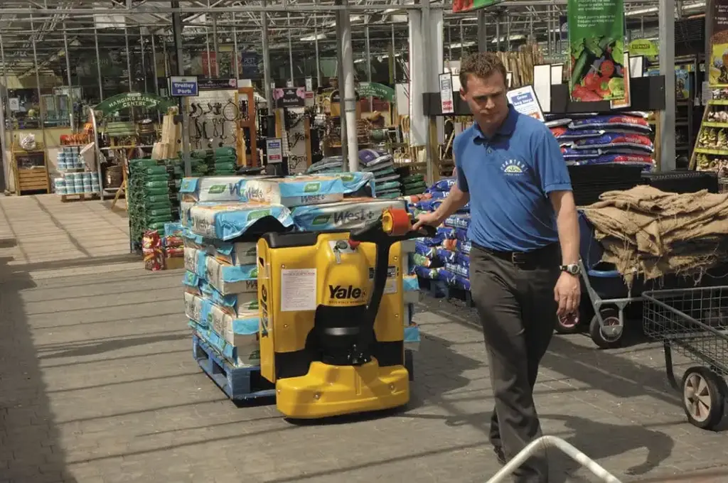 A man using a Yale MPW pallet mover to transport a pallet of goods through a garden store.