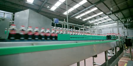Staring down a long assembly line with blurred bottles of pop in a bottling facility.