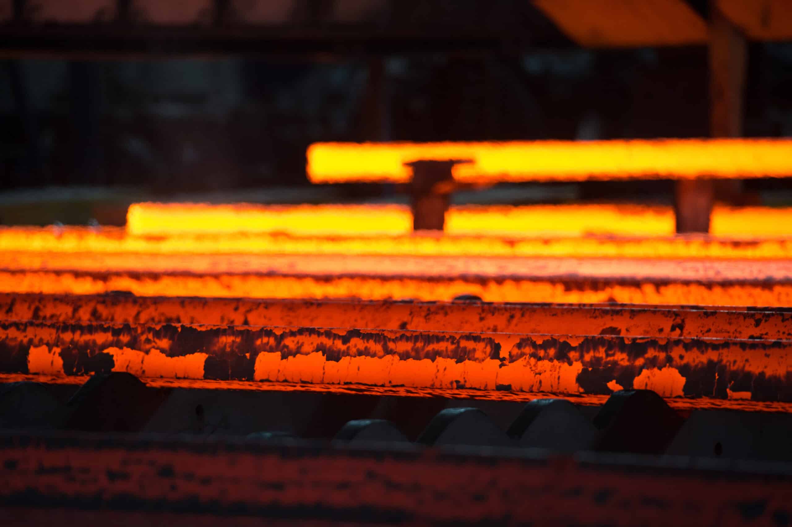 Glowing hot steel bars in a row, illuminated and radiant in the heat of a steel mill.