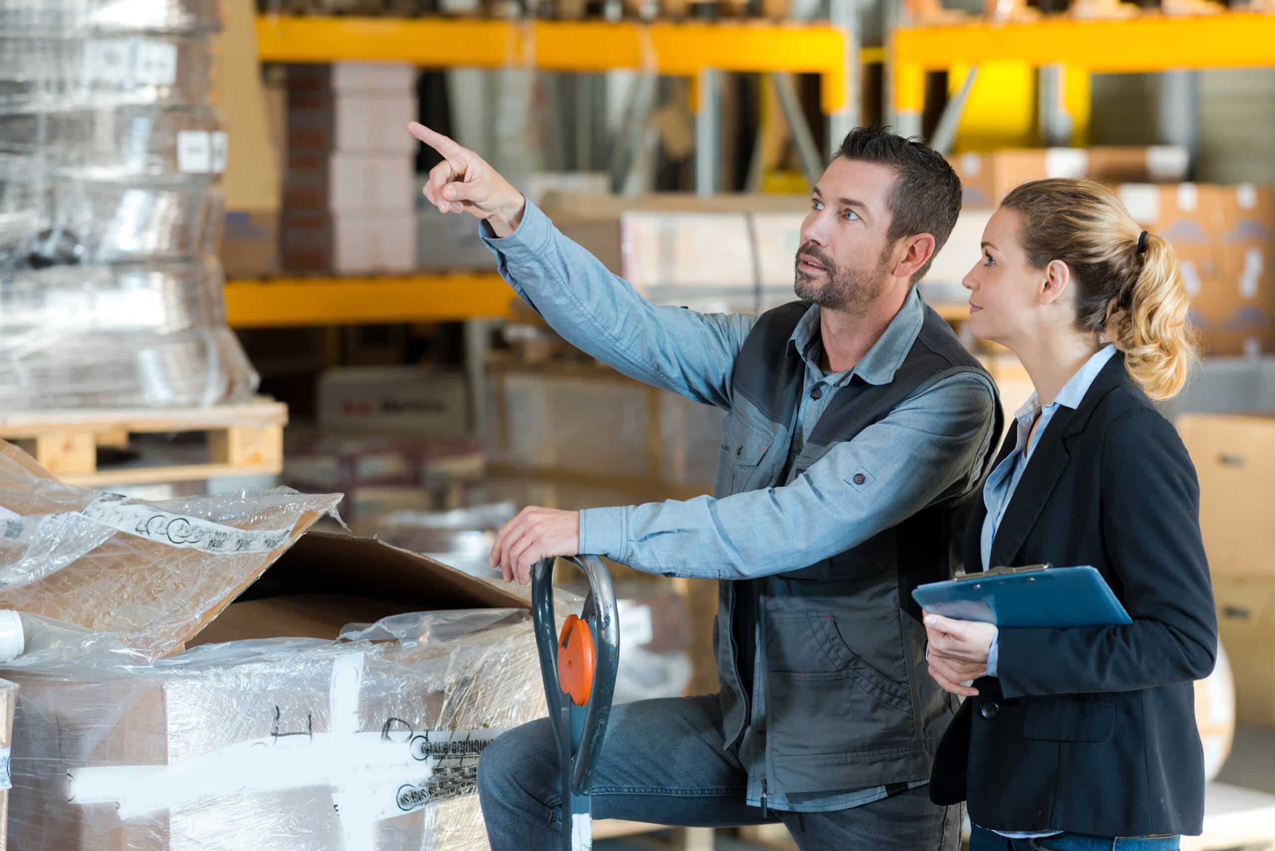Warehouse manager pointing out something to a colleague with a clipboard in a storage facility.