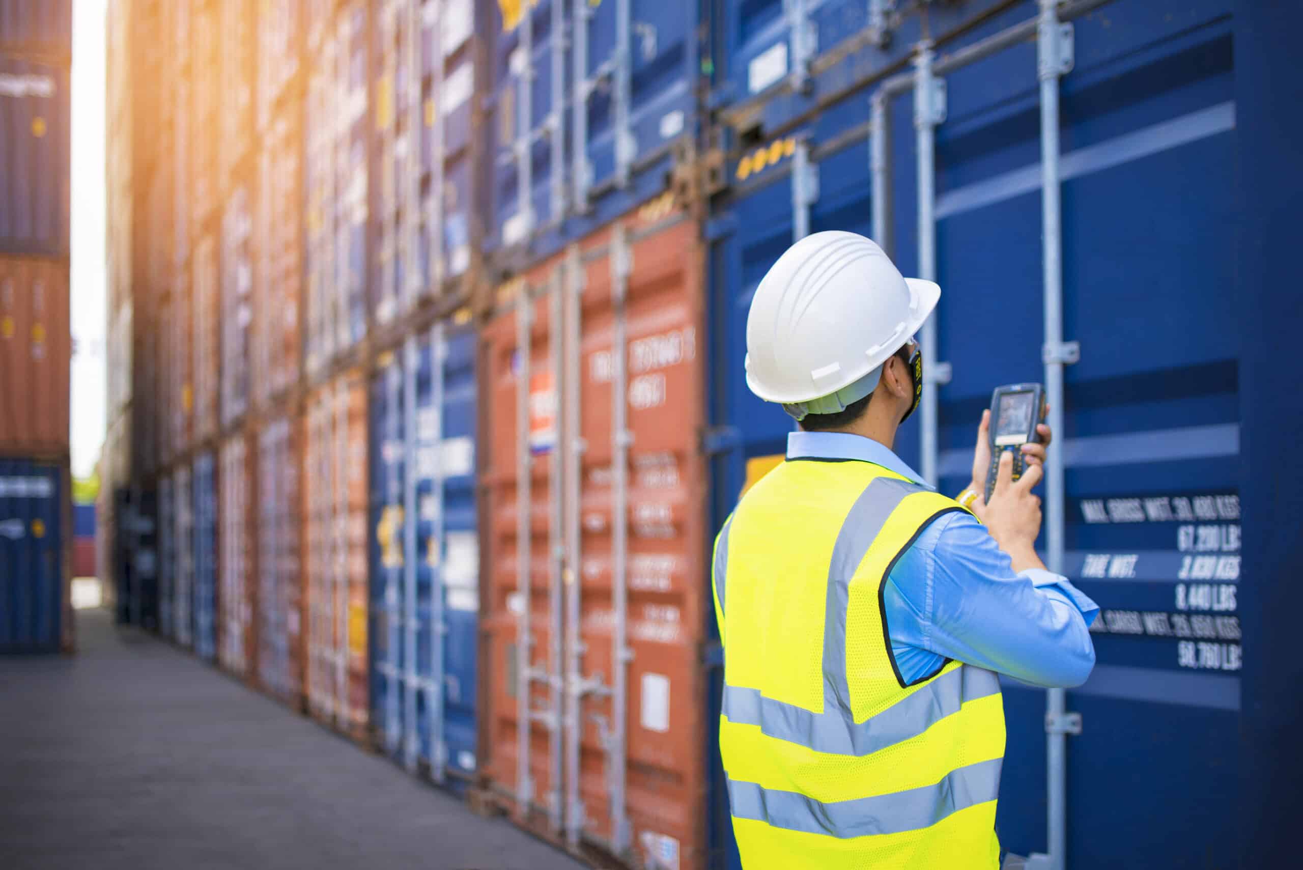 A material handling professional in a safety vest and hard hat using a handheld device to manage inventory.