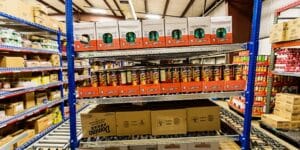 A warehouse shelf stocked with assorted boxes, including food. The shelving unit has blue vertical beams and rollers on the bottom to let cases slide.