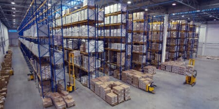 Overhead view of a warehouse with 9 rows of blue racking filled with pallets of inventory and 5 yellow forklifts in sight transporting goods.