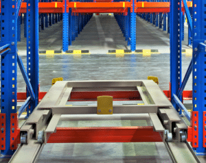 View from inside blue metal racking that has a platform that can move back to store goods in a warehouse. Racking is currently empty so viewer can see down entire rows.
