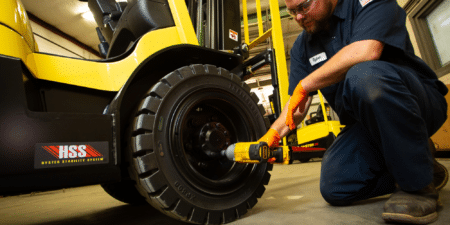 Technician holding a drill that is securing bolts on a tire of a yellow forklift in a warehouse.