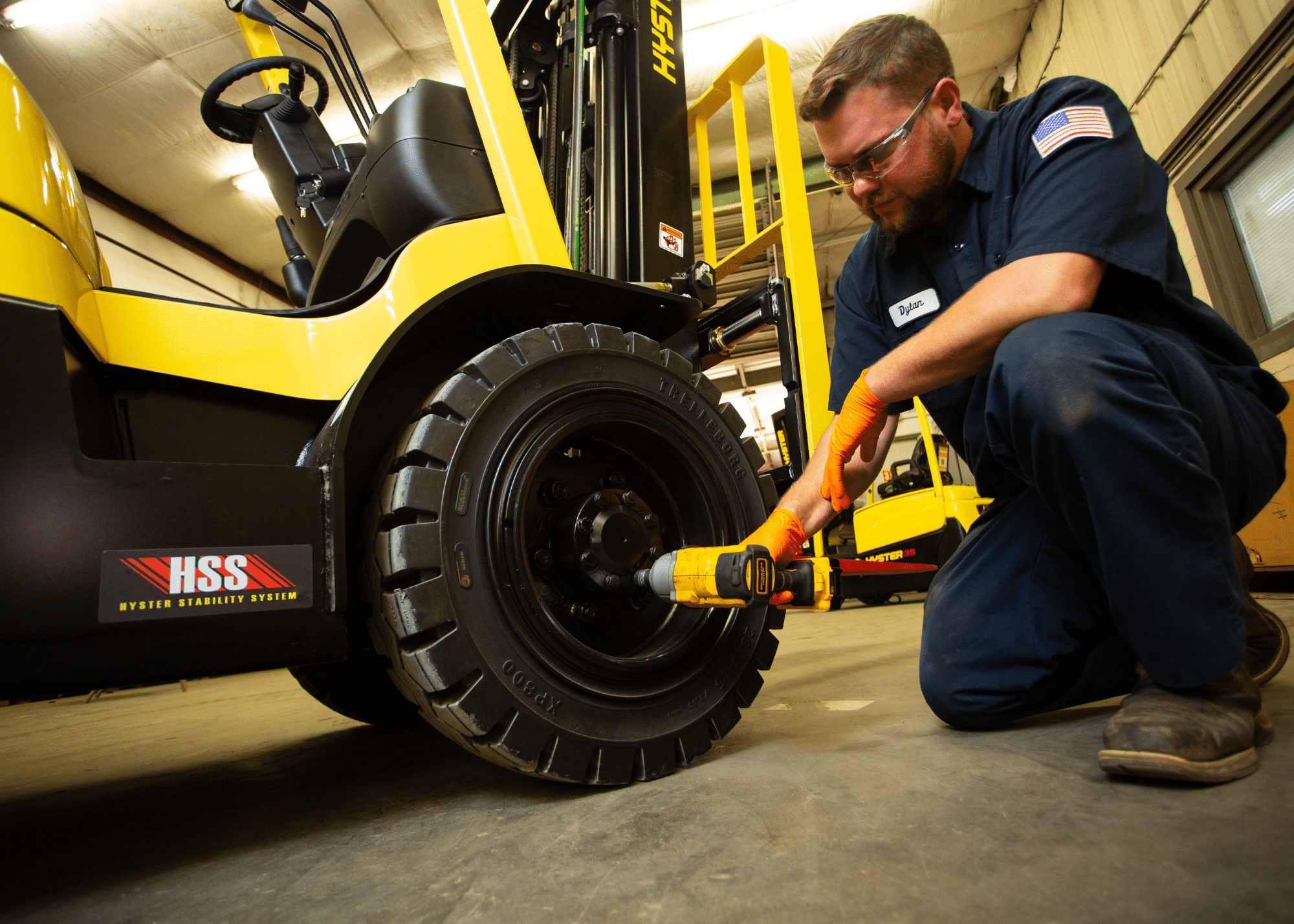 Technician holding a drill that is securing bolts on a tire of a yellow forklift in a warehouse.