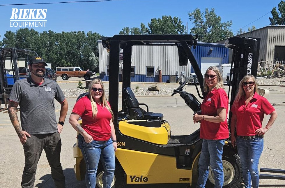 Four Riekes team members standing in front of a yellow Yale forklift smiling for a picture.