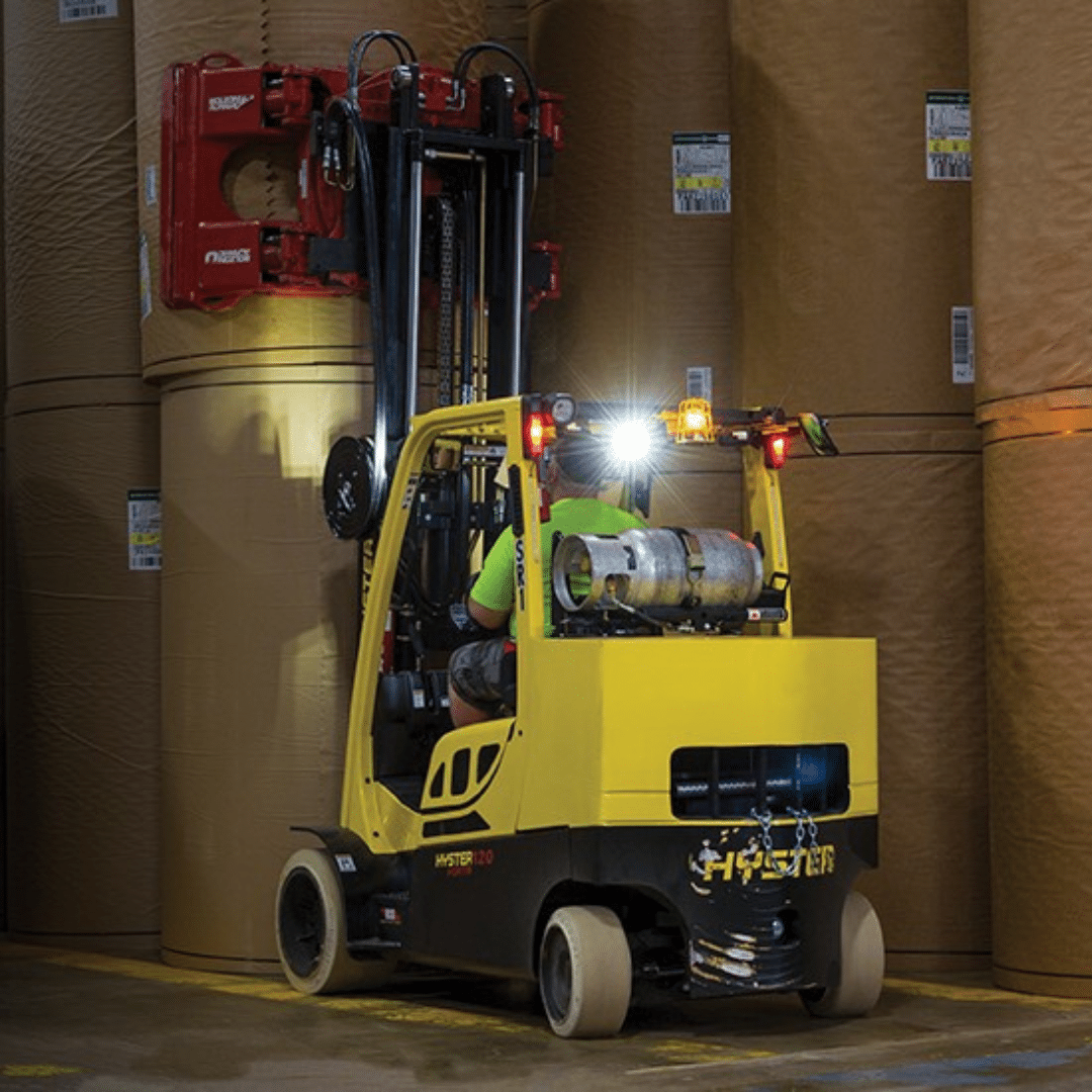 Hyster forklift with paper roll clamp in a dark warehouse stacking large rolls of paper.