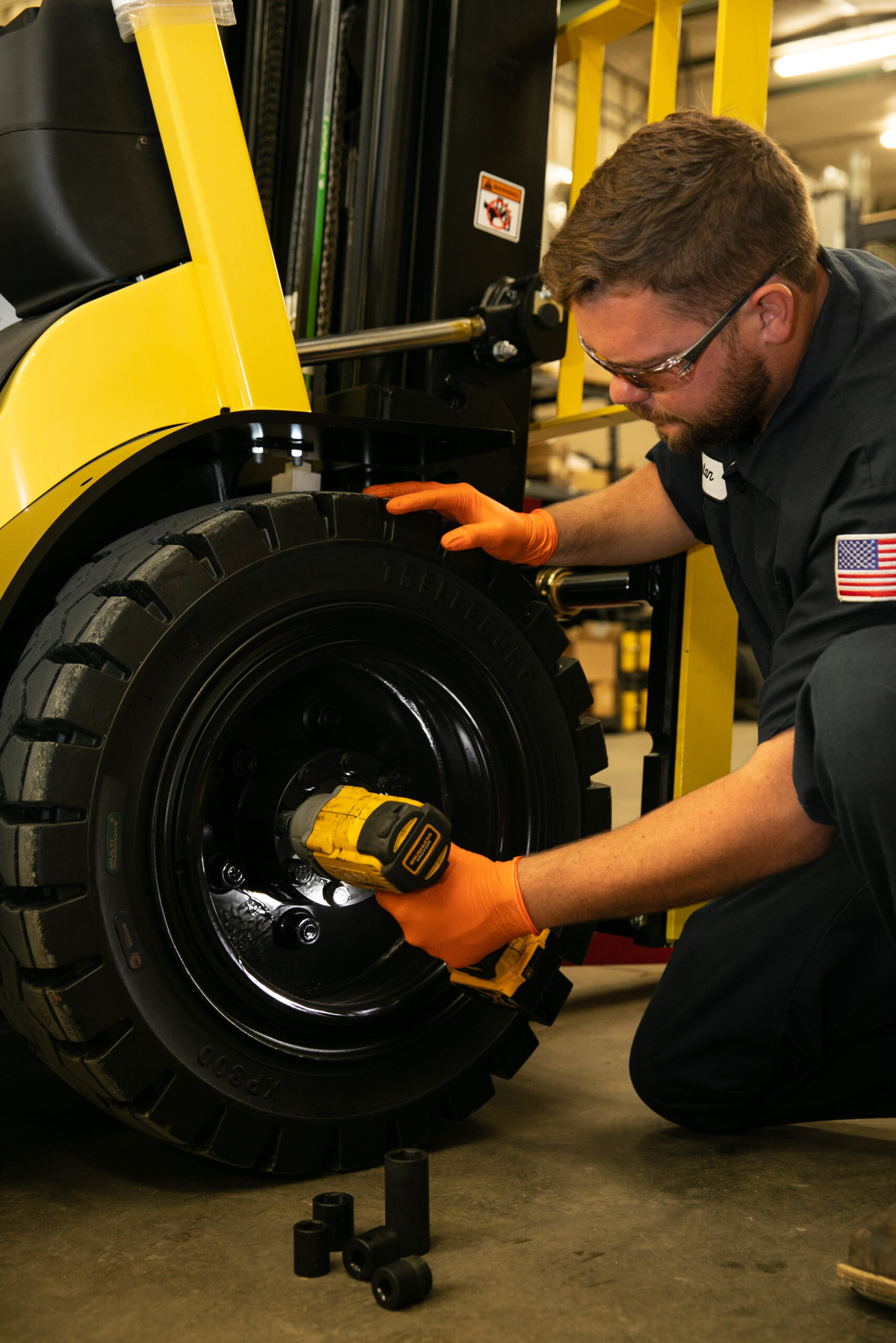 Forklift technician kneeling down to fix a forklift tire