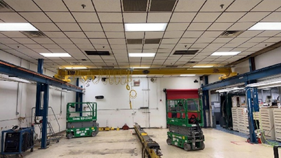 image of a small warehouse with a low ceiling, showcasing their new overhead crane system traversing the space.