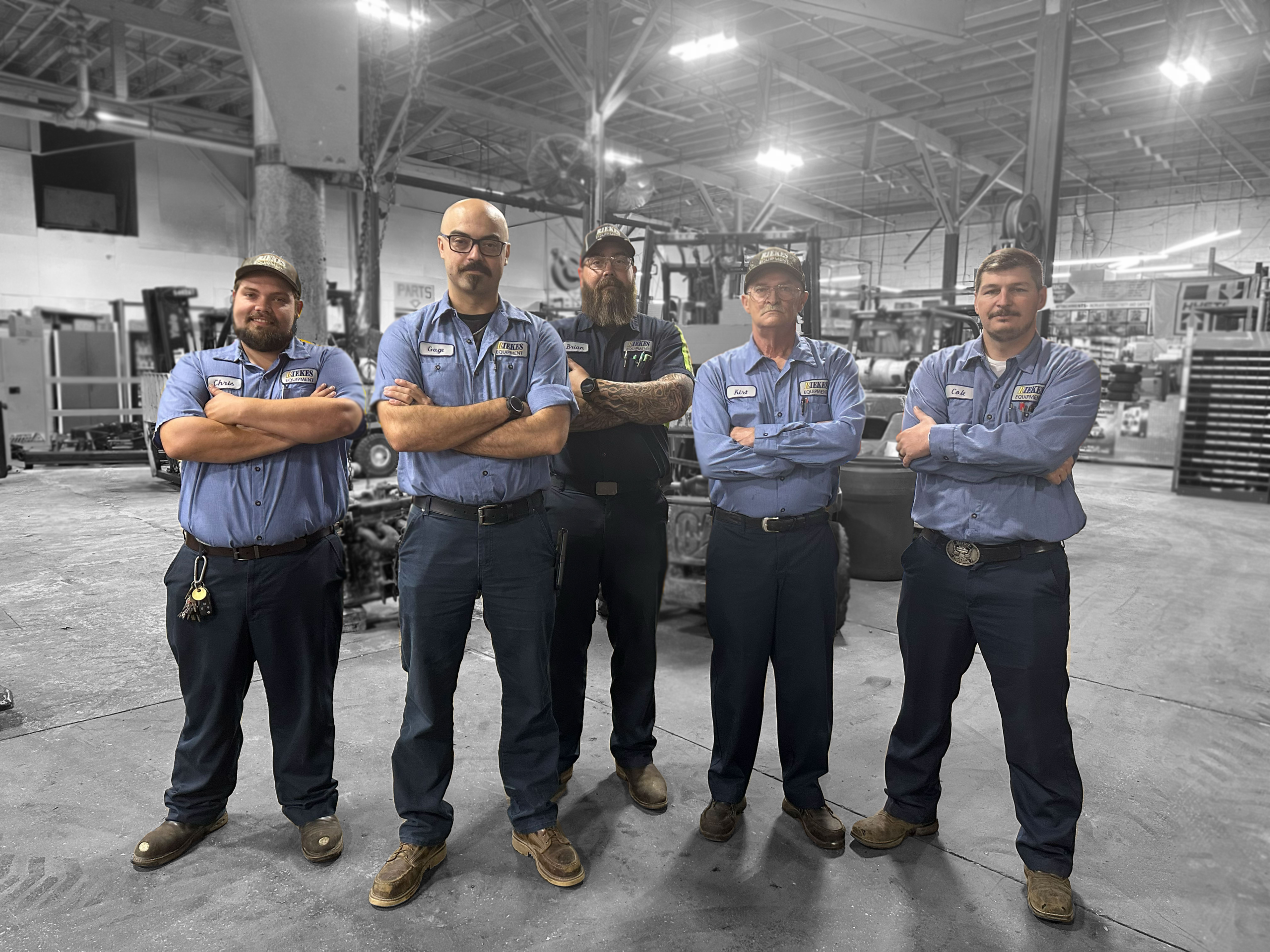 Five men in service uniforms standing in a mechanic shop by a forklift