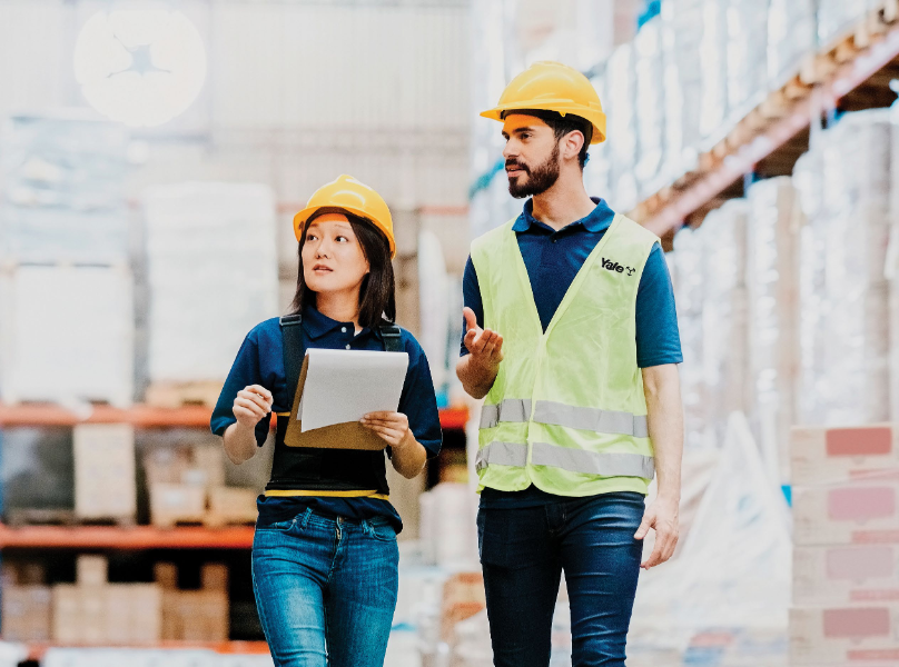 a man and a women in safety gear walking around a warehouse inspecting operations