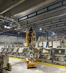 image of a warehouse worker on a scissor lift that is elevated near the ceiling to install a vacuum lift system for a pet food manufacturer.