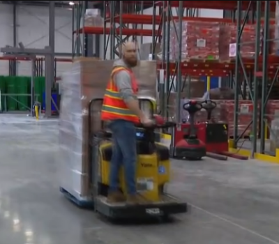 A guy moving through a warehouse on an end rider fork truck.