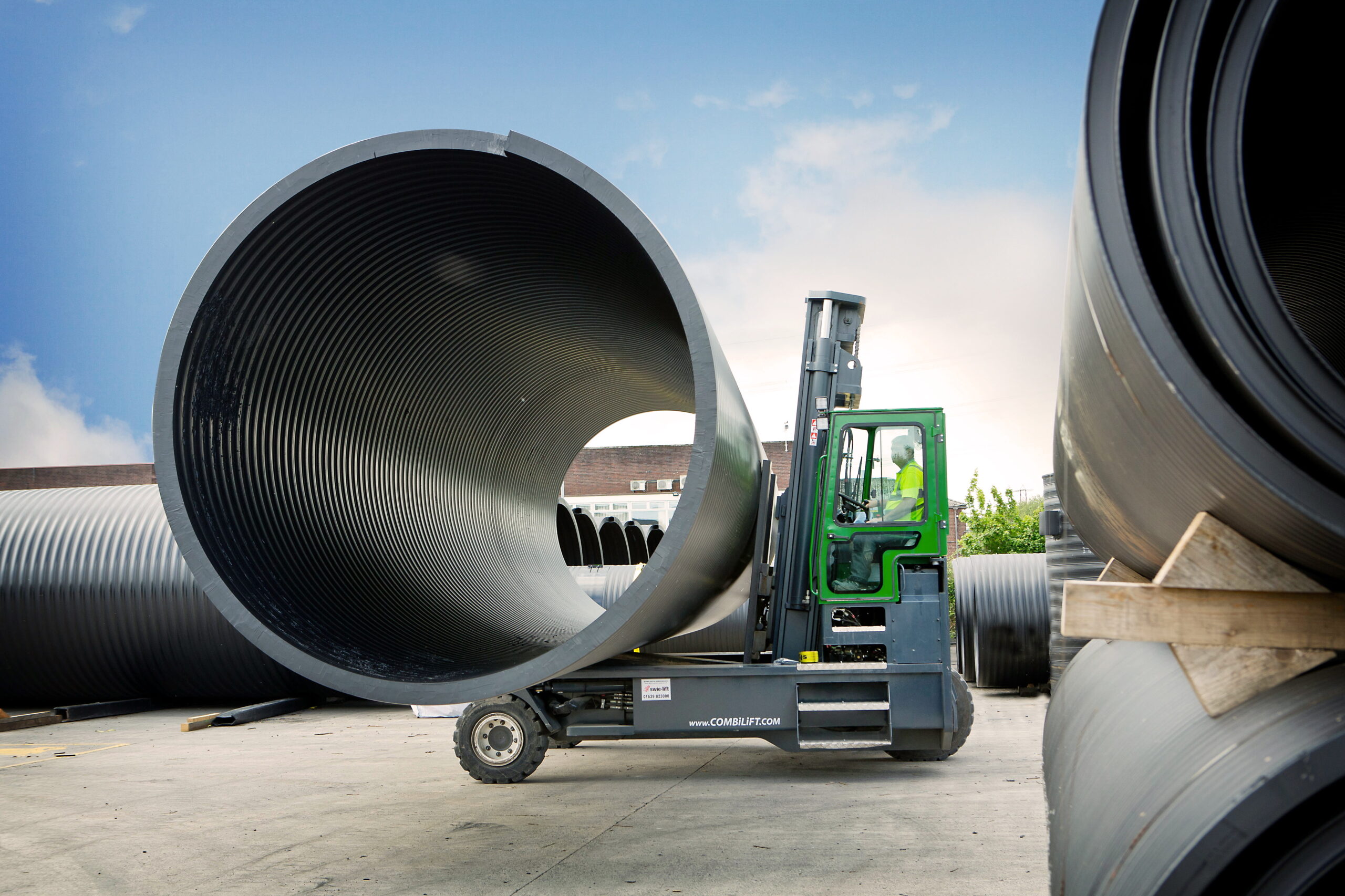 Combilift forklift side view of truck moving large,metal pipe